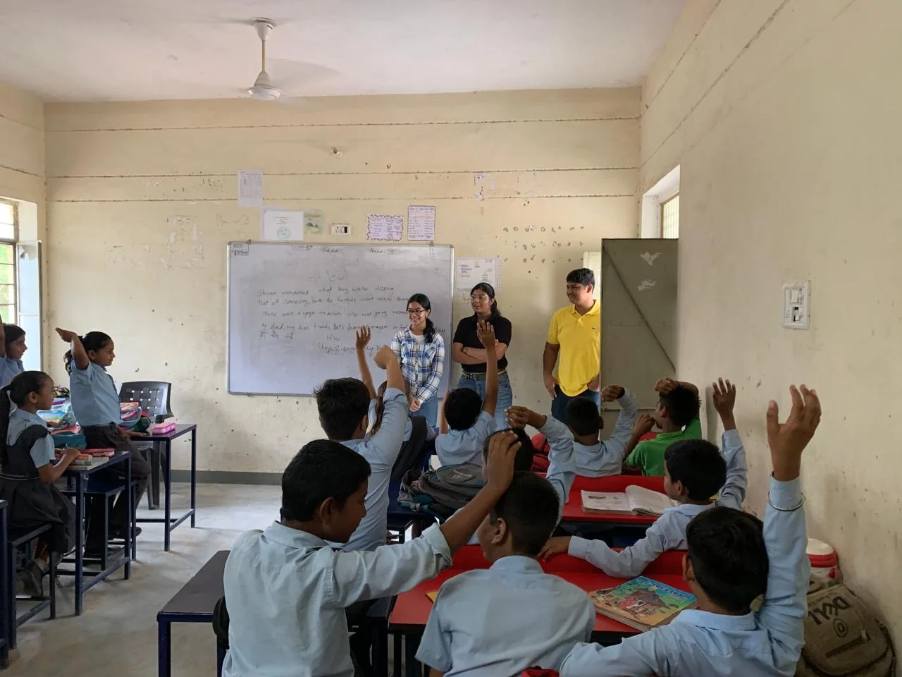 Myra Jhawar and volunteers at the front of a classroom as students raise their hands
