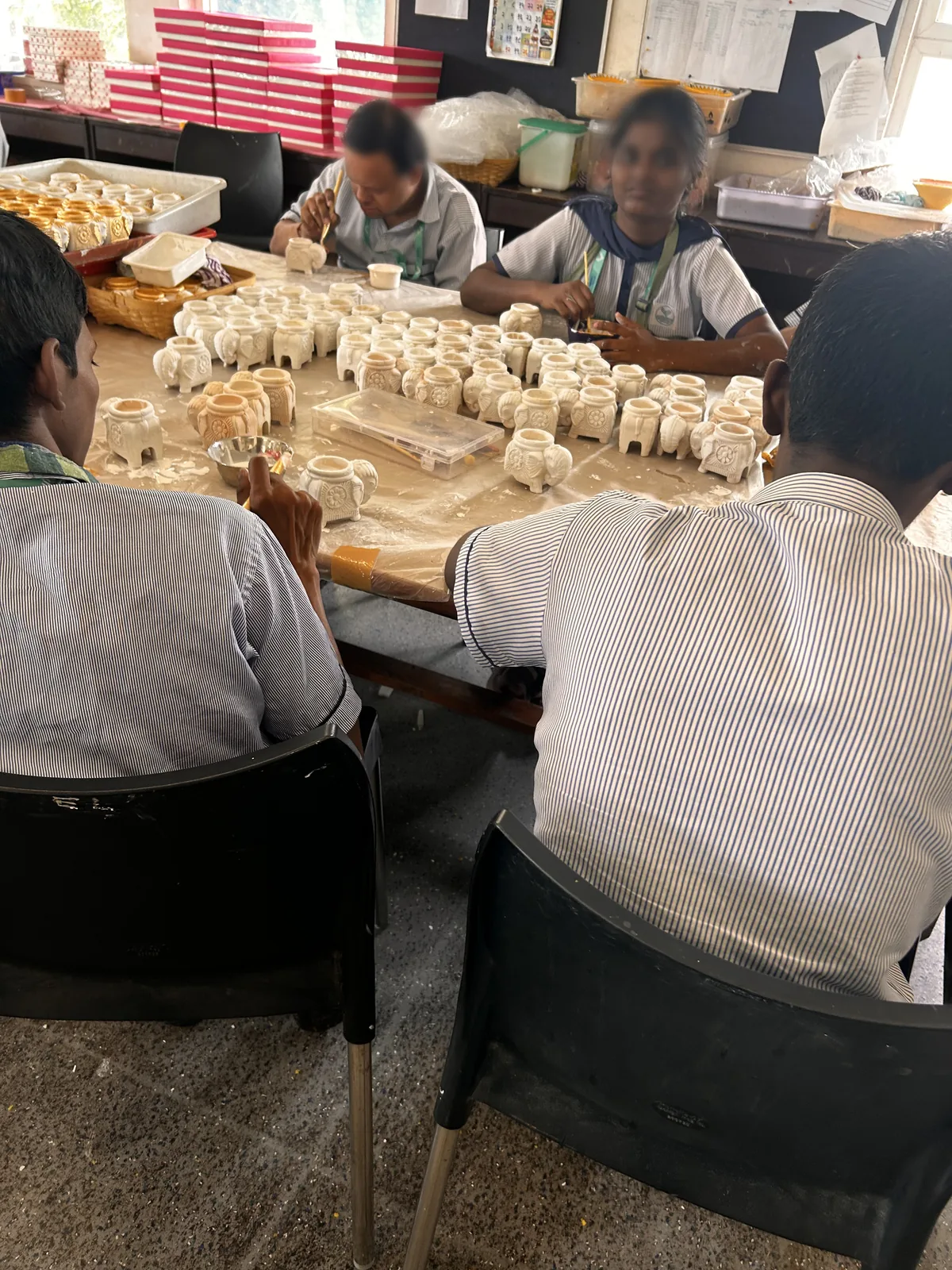 Trainees working on handcrafted pieces at a Jai Vakeel Foundation workshop table, faces blurred
